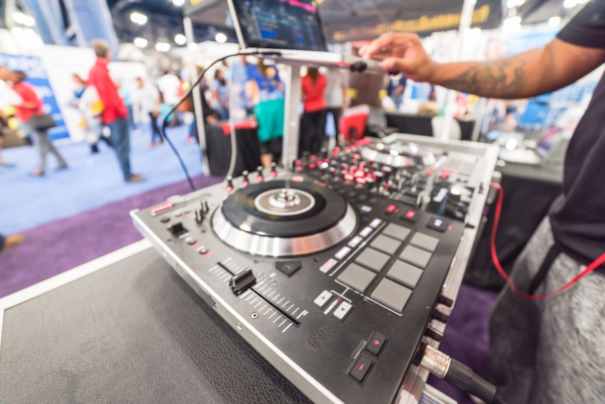 Blurred tattoo hand of DJ mixing music on laptop with turntable controller at conventional hall/expo event fair. DJ mixing tracks, music festival and entertainment concept. Defocused background bokeh